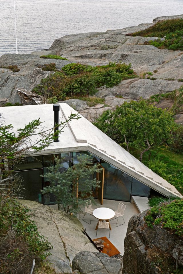Half-hidden by dense vegetation, this modern cabin is tucked into a rocky Norwegian coastline. It is a 323 sq ft studio design with a sleeping loft suspended from the ceiling. | www.facebook.com/SmallHouseBliss